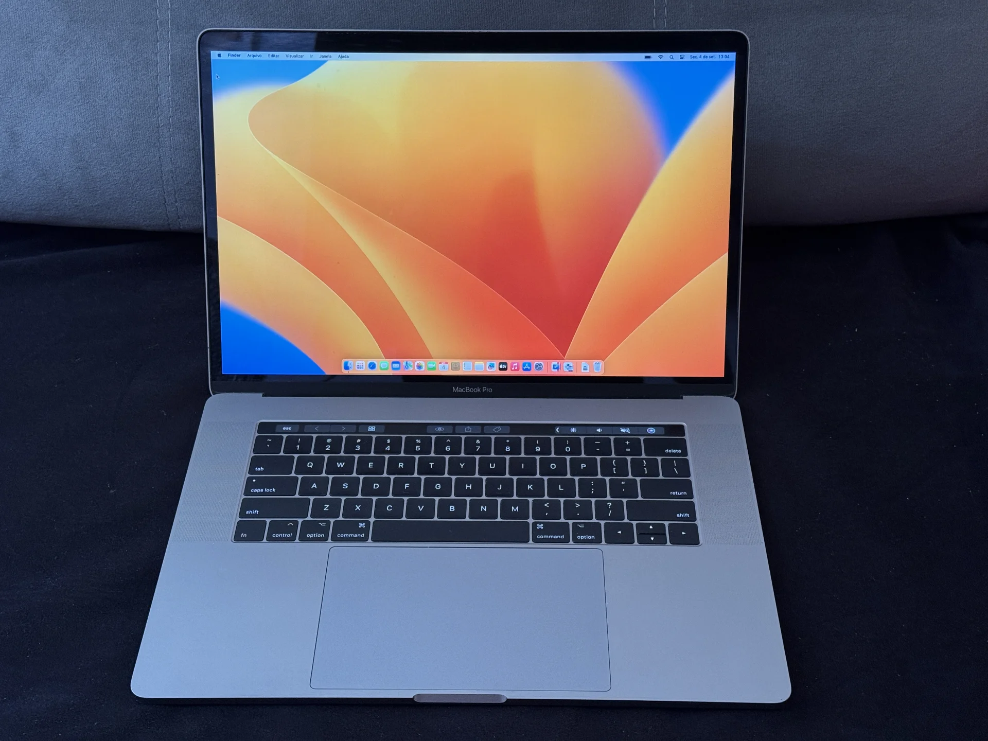 MacBook Pro aberto, com tela ligada, teclado, Touch Bar e trackpad visíveis.